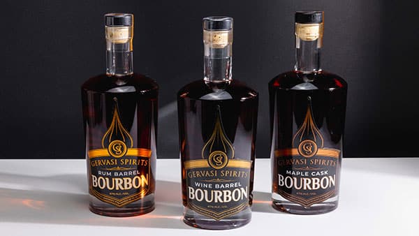 Lineup of Gervasi Spirits bourbon bottles including Rum Barrel, Wine Barrel, and Maple Cask on a white surface with black background.