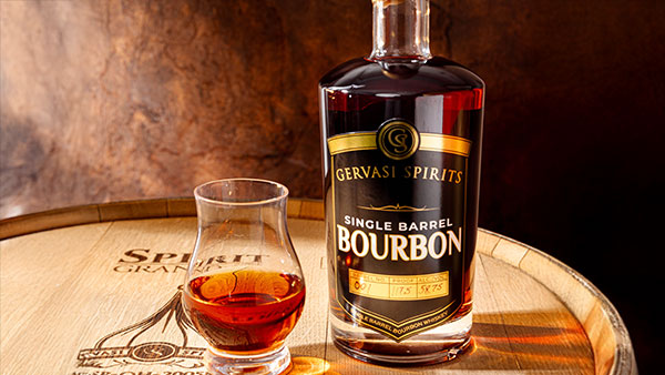 Gervasi Spirits Single Barrel Bourbon bottle with tasting glass displayed on oak barrel under warm lighting
