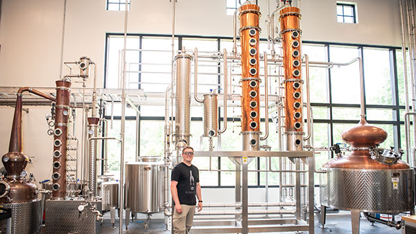 Gervasi Vineyard’s advanced distillery showcasing gleaming copper column stills and stainless-steel tanks, with a master distiller on site crafting small-batch spirits like Sinner’s Blush rosé vodka for refined cocktails and artisan martinis.