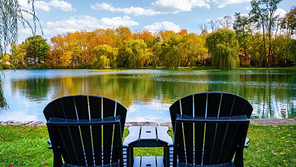 Two black Adirondack chairs overlooking a serene lake surrounded by colorful fall foliage at Gervasi Vineyard