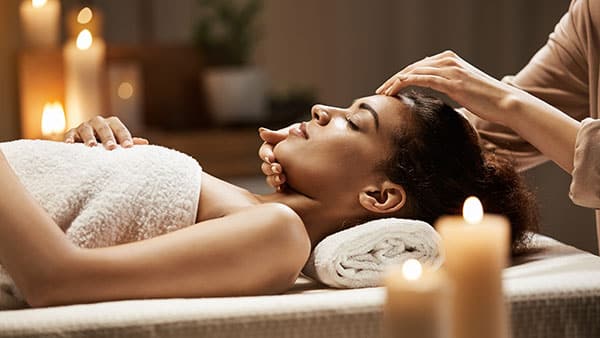 Woman receiving a relaxing facial massage at The Spa at Gervasi Vineyard surrounded by warm candlelight.