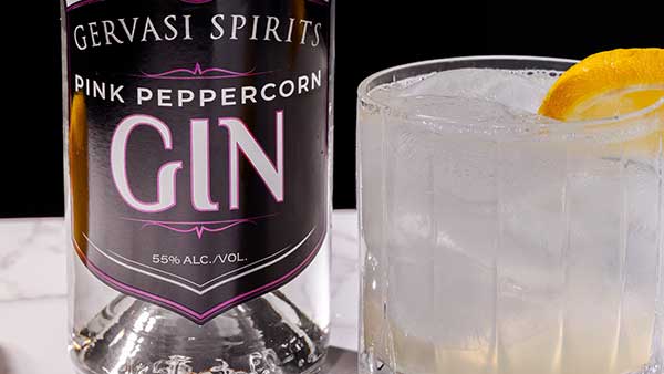 Close-up of a classic gin cocktail with lemon, featuring Gervasi Spirits Pink Peppercorn Gin bottle.