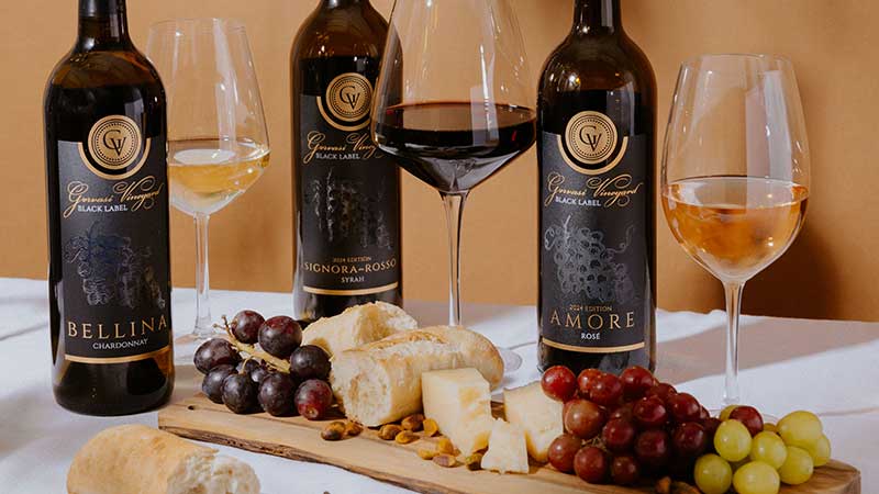 A curated tasting display of Gervasi Vineyard’s Black Label Collection—Bellina Chardonnay, Signora Rosso Syrah, and Amore Rosé—accompanied by wine glasses, bread, and cheese, perfect for elevated summer gatherings.