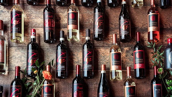 Assorted bottles of Gervasi Vineyard wine displayed on a rustic wood background with floral accents.